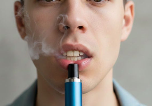 Close-up of a person exhaling vapor from an e-cigarette, with mildly stained teeth.